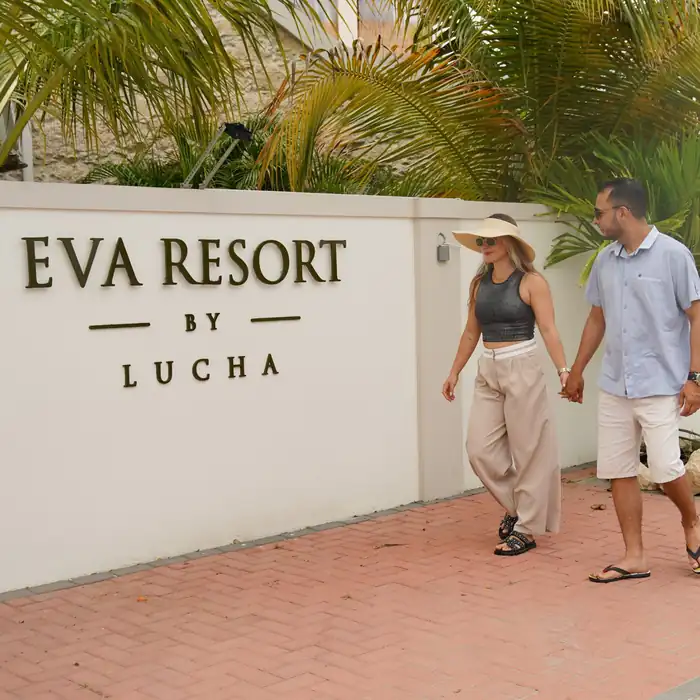 Couple walking past the EVA Resort by Lucha entrance sign in Savaneta, Aruba